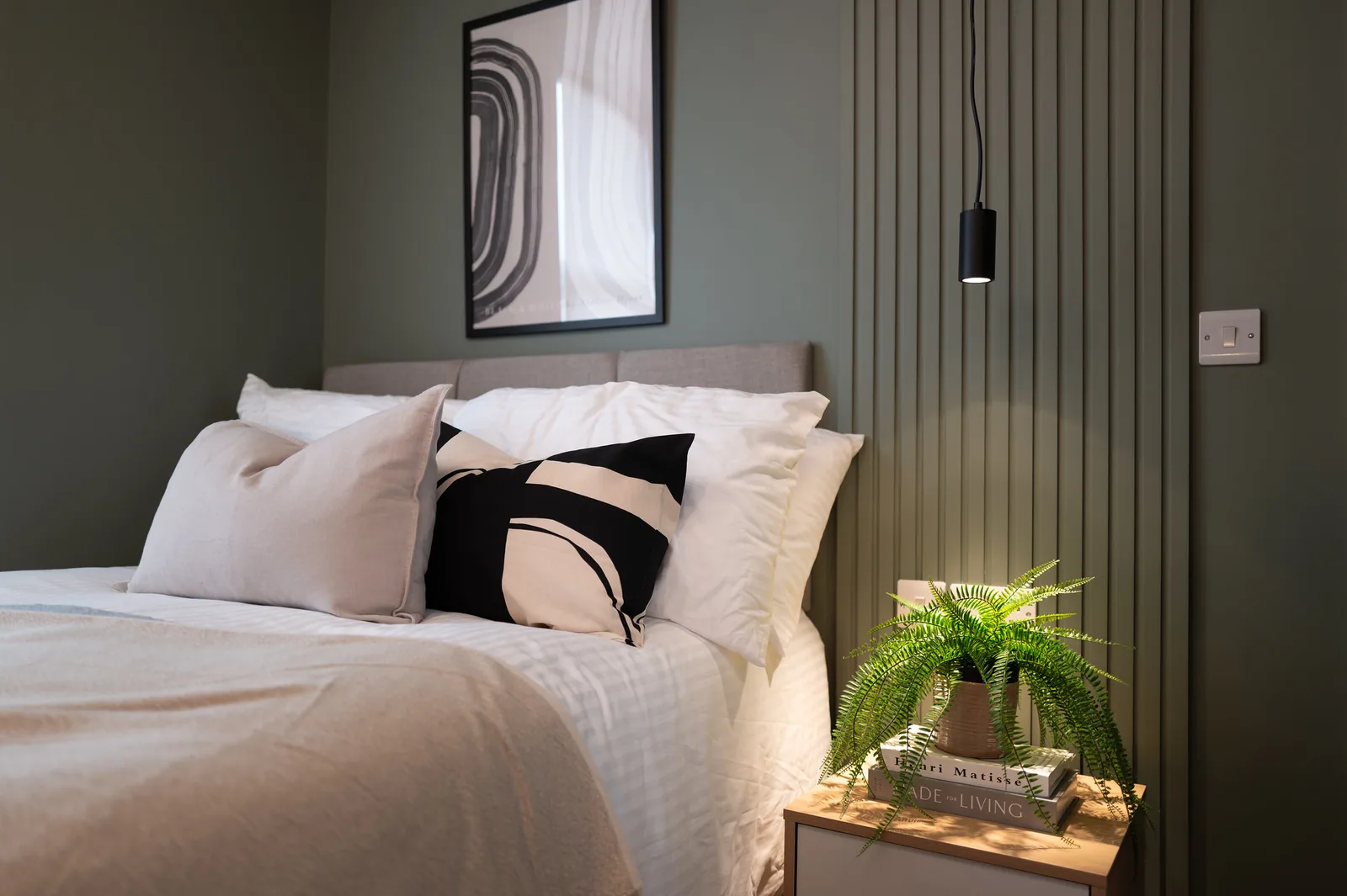 Warm bedroom interior with a green wall, upholstered bed and fern